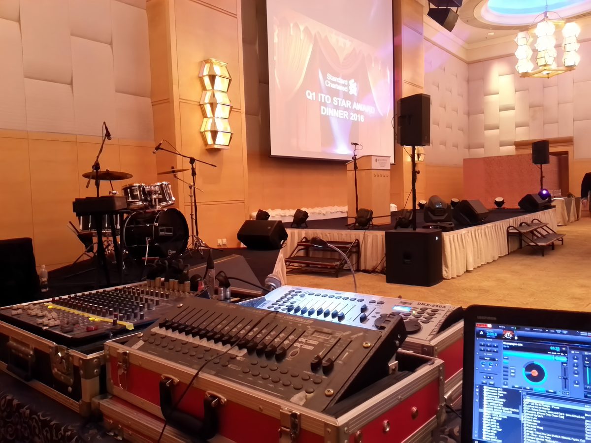 Lighting desk, mixer and DJ rig at front of house facing an awards-dinner stage