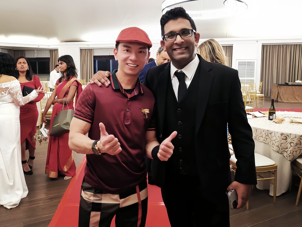 William with a smiling host at a wedding reception, both giving thumbs up