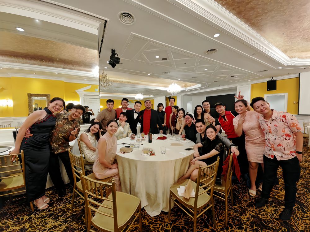 A full table of guests posing together at an annual dinner in a gold ballroom