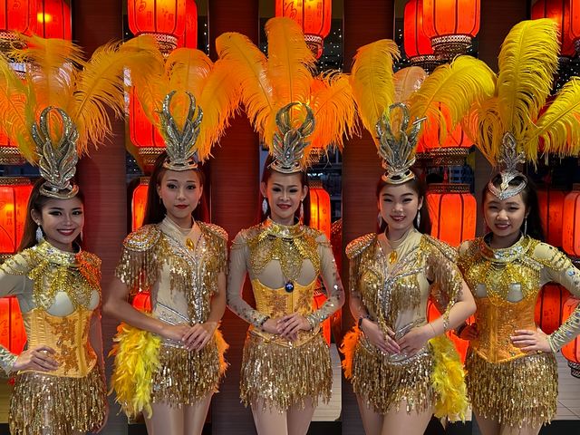 Troupe in gold and feather headdresses before a red-lantern backdrop