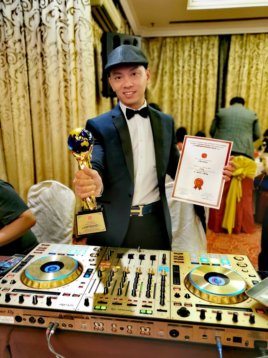 DJ Will in black tie holding the trophy and certificate beside his decks