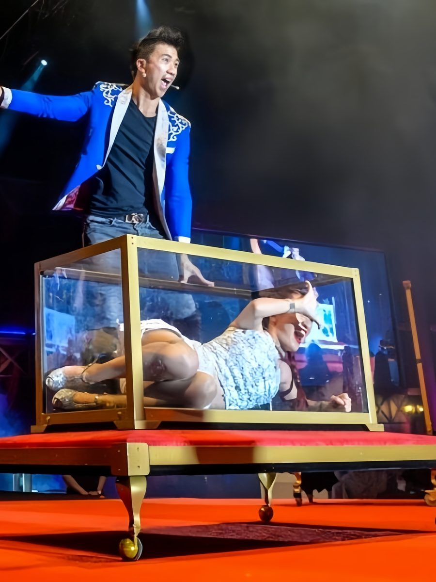 Illusionist mid-act over a glass box on stage
